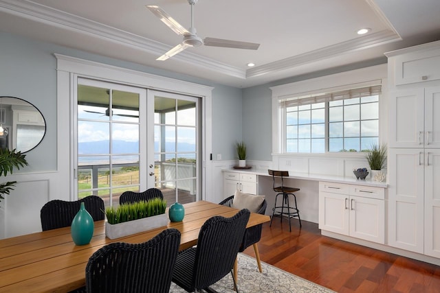 dining room featuring dark wood-style flooring, a ceiling fan, french doors, a tray ceiling, and ornamental molding