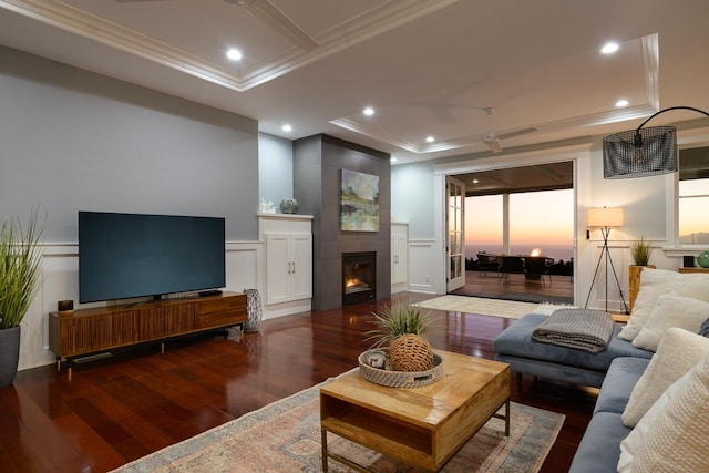 living room with a raised ceiling, wood finished floors, a decorative wall, and ornamental molding