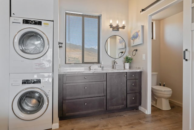 laundry room with a barn door, light wood-style floors, stacked washer / dryer, and a sink