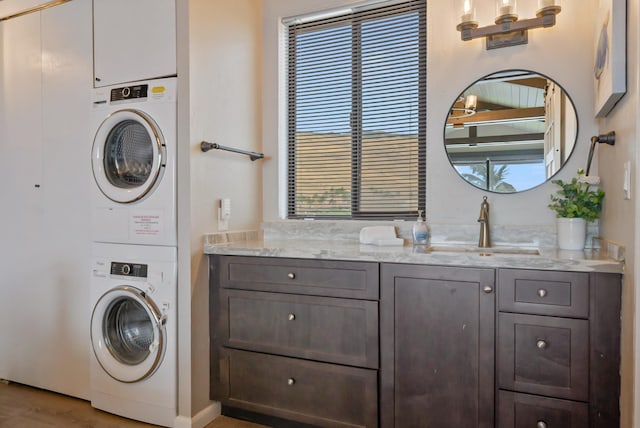 clothes washing area featuring stacked washer and clothes dryer, a sink, and cabinet space