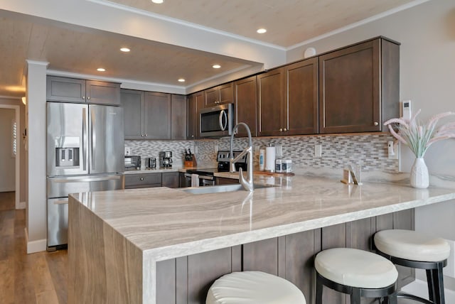 kitchen featuring light stone counters, light wood-style floors, dark brown cabinetry, stainless steel appliances, and a peninsula