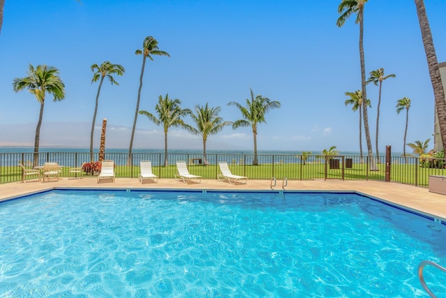 community pool featuring fence, a patio, and a water view