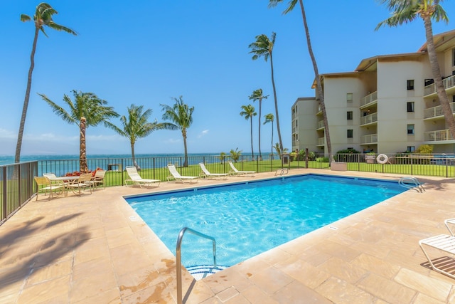 community pool featuring fence, a water view, and a patio area