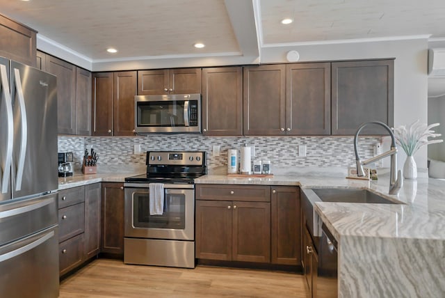 kitchen with crown molding, a sink, stainless steel appliances, light wood finished floors, and light stone countertops