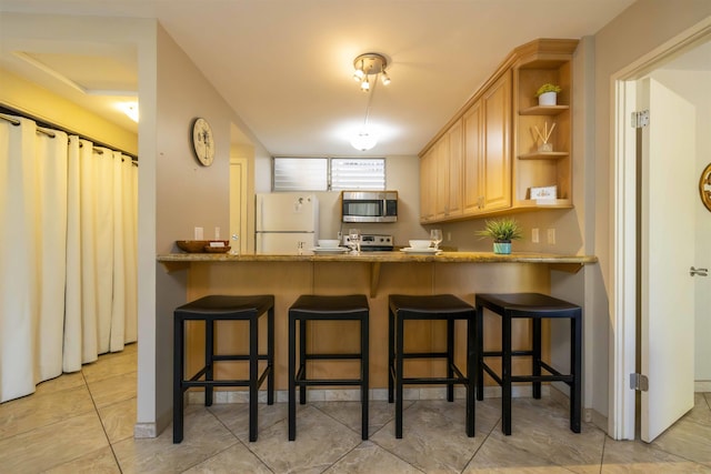 kitchen with stainless steel appliances, stone countertops, a kitchen breakfast bar, and light brown cabinetry