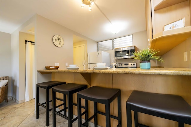 kitchen with appliances with stainless steel finishes, a kitchen bar, and light tile patterned flooring