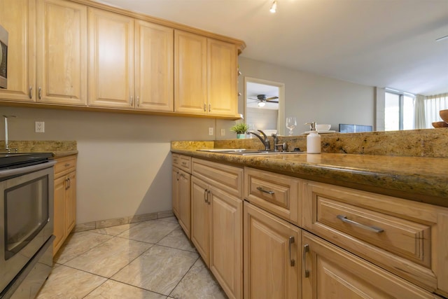 kitchen with appliances with stainless steel finishes, ceiling fan, dark stone counters, light brown cabinetry, and sink