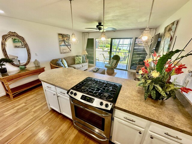 kitchen with light wood-type flooring, gas stove, ceiling fan, and white cabinets