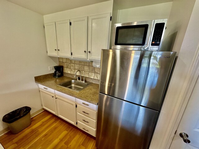 kitchen featuring appliances with stainless steel finishes, light hardwood / wood-style flooring, white cabinetry, tasteful backsplash, and sink