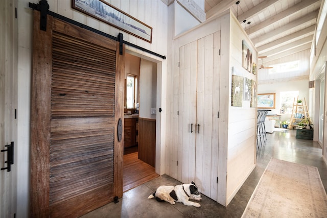 hall with wooden walls, vaulted ceiling with beams, a barn door, and concrete flooring