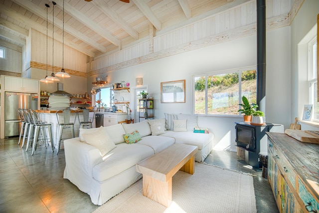 living room featuring high vaulted ceiling, ceiling fan, wood ceiling, a wood stove, and beam ceiling