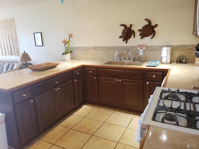 kitchen featuring kitchen peninsula, backsplash, sink, light tile floors, and stove