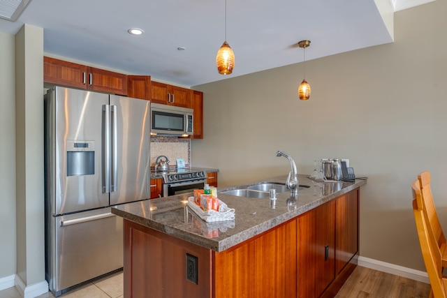 kitchen with dark stone counters, light hardwood / wood-style flooring, stainless steel appliances, decorative light fixtures, and sink