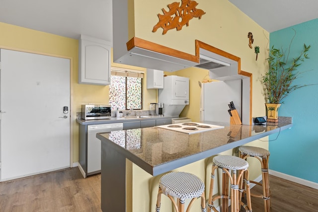 2219 S Kihei Rd Unit B312, Kihei, HI 96753 - kitchen featuring stacked washing machine and dryer, white appliances, wood finished floors, white cabinets, and a breakfast bar