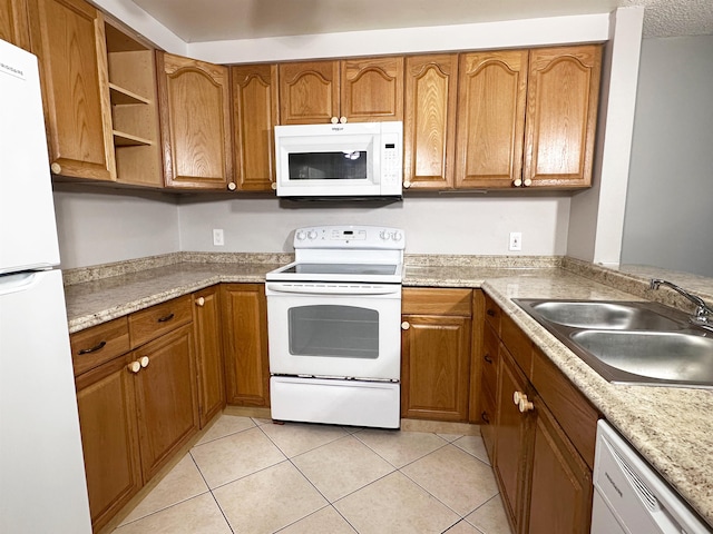 kitchen with light tile patterned flooring, white appliances, light stone countertops, and sink