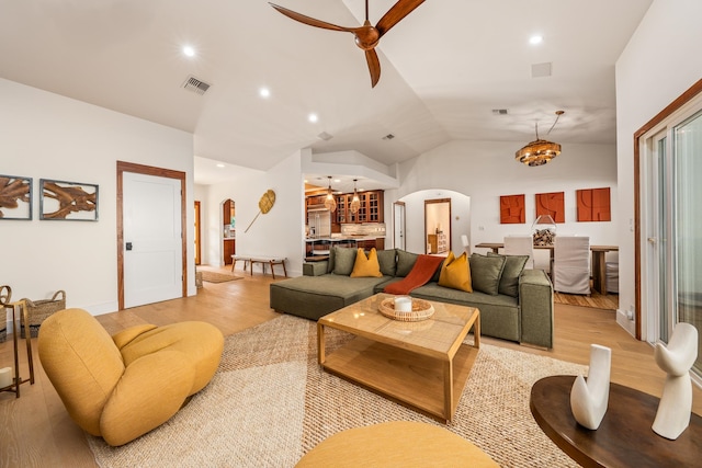 living room featuring light hardwood / wood-style flooring, ceiling fan with notable chandelier, and vaulted ceiling