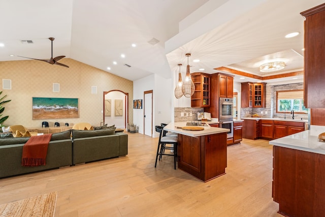 kitchen featuring ceiling fan, hanging light fixtures, stainless steel double oven, light hardwood / wood-style flooring, and kitchen peninsula