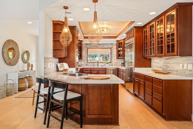 kitchen featuring stainless steel appliances, tasteful backsplash, kitchen peninsula, pendant lighting, and light wood-type flooring