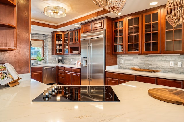 kitchen featuring hanging light fixtures, decorative backsplash, a tray ceiling, light stone counters, and stainless steel appliances