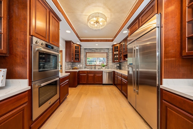 kitchen featuring a raised ceiling, sink, light hardwood / wood-style flooring, decorative backsplash, and appliances with stainless steel finishes