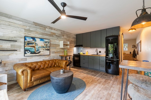 kitchen with wood walls, sink, black appliances, and light hardwood / wood-style flooring