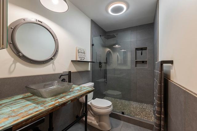 bathroom featuring tile patterned flooring, tiled shower, toilet, and sink