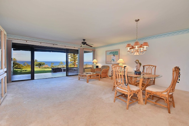 carpeted dining space featuring ceiling fan with notable chandelier and a water view