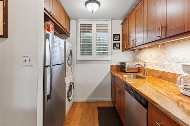 kitchen with stainless steel appliances, stacked washer / dryer, sink, and light stone counters