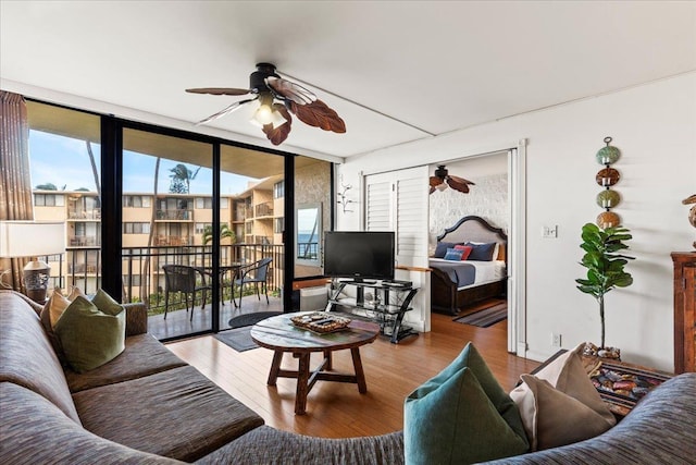 living room featuring ceiling fan, a wall of windows, and wood-type flooring