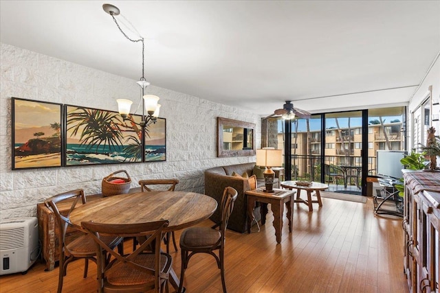 dining room with floor to ceiling windows, ceiling fan with notable chandelier, and hardwood / wood-style floors