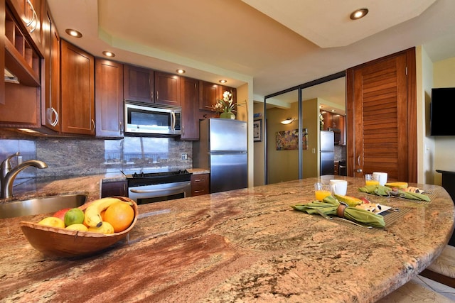 kitchen featuring a kitchen breakfast bar, sink, light stone countertops, appliances with stainless steel finishes, and tasteful backsplash