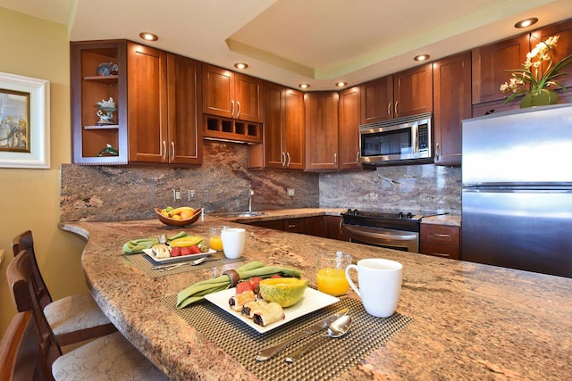 kitchen featuring stainless steel appliances, light stone counters, kitchen peninsula, a breakfast bar area, and decorative backsplash