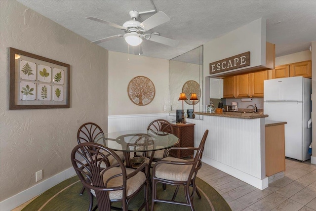 dining space featuring ceiling fan, sink, a textured ceiling, and light hardwood / wood-style flooring