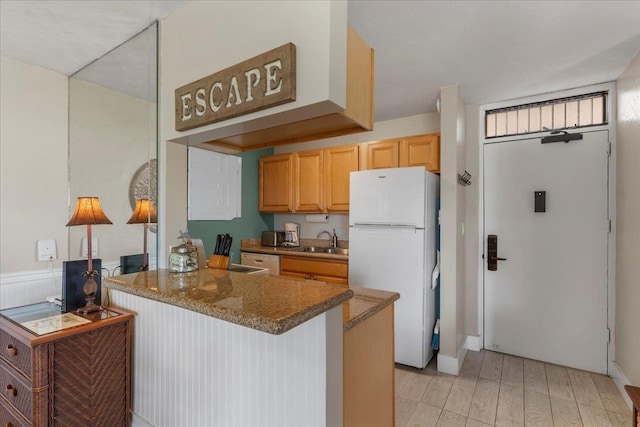 kitchen with kitchen peninsula, white refrigerator, light hardwood / wood-style flooring, and dark stone counters