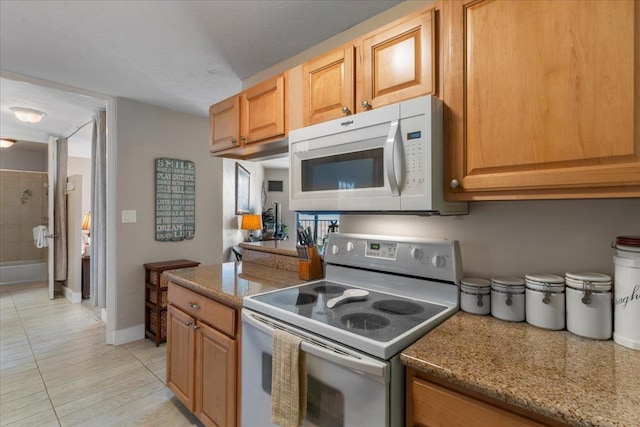 kitchen featuring light tile patterned flooring, light stone counters, and white appliances