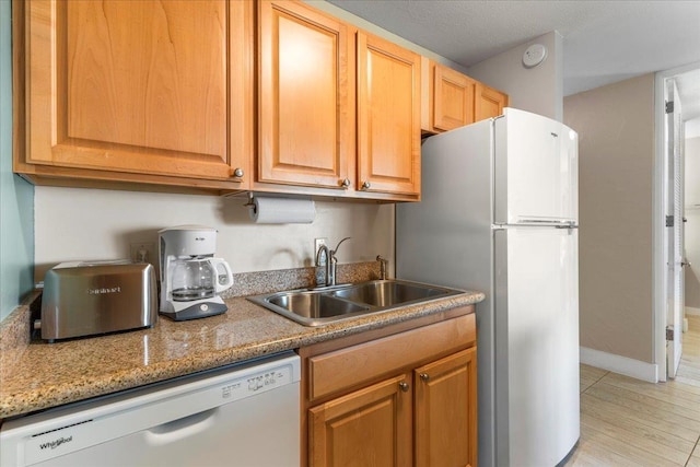 kitchen featuring stainless steel refrigerator, light stone countertops, dishwasher, and sink