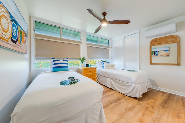 bedroom with a closet, light wood-type flooring, a wall unit AC, and ceiling fan