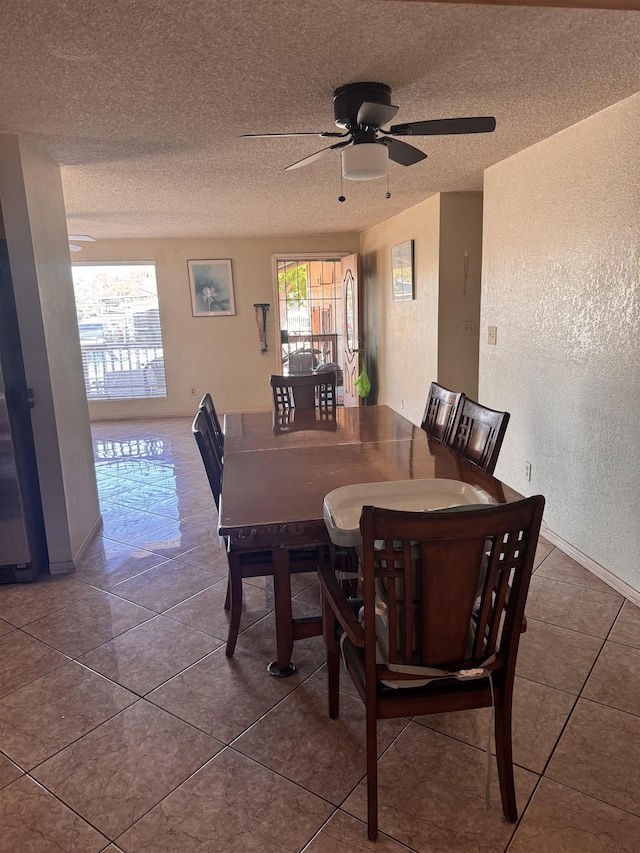 dining area featuring tile patterned floors, a ceiling fan, a textured wall, and a textured ceiling