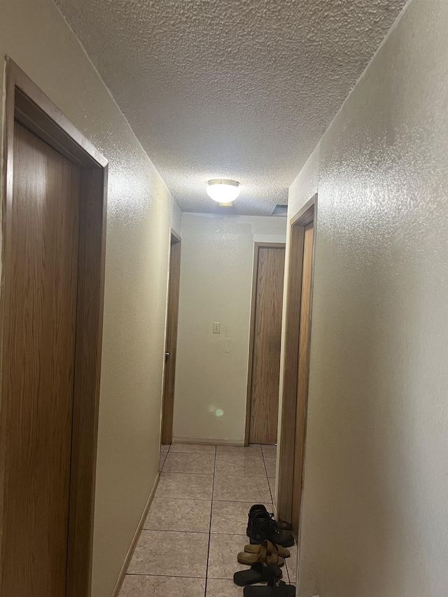 hall with light tile patterned floors, a textured ceiling, and a textured wall