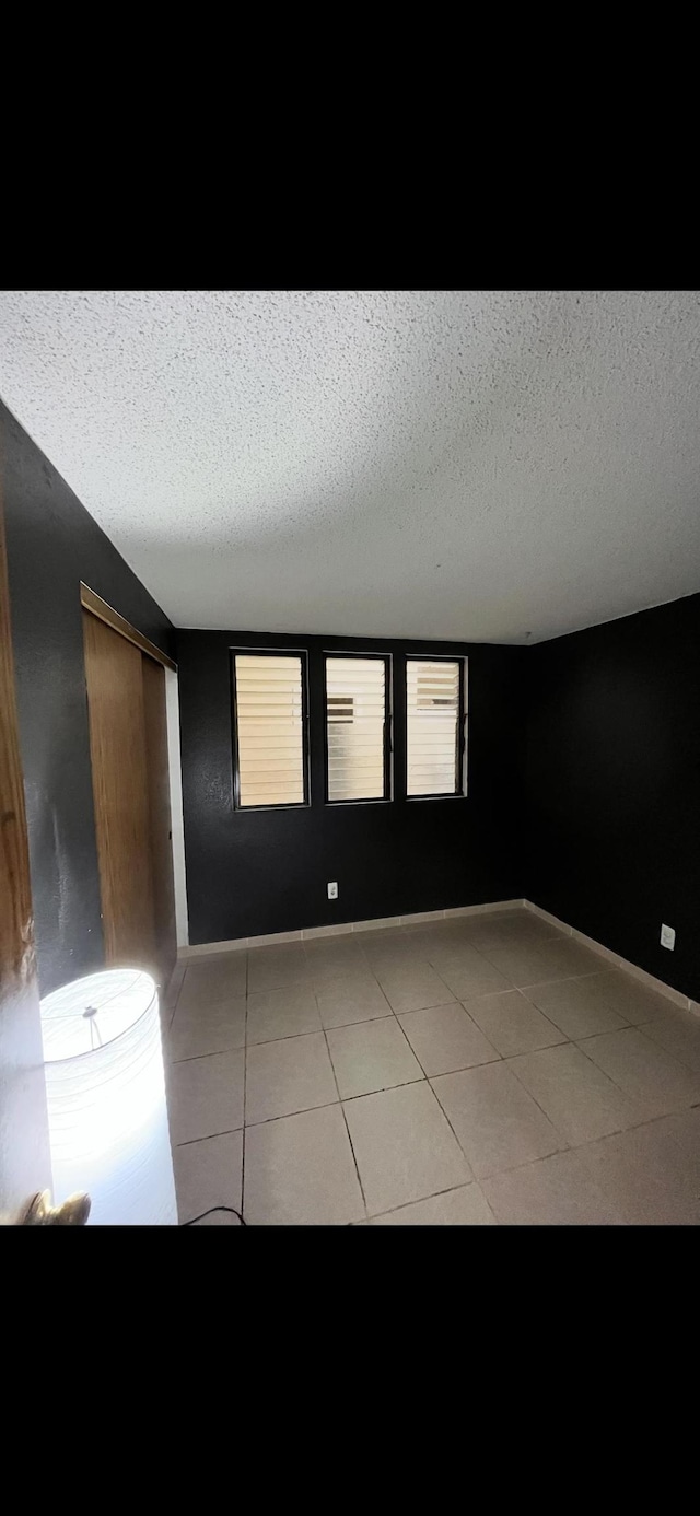 spare room featuring light tile patterned floors, a textured ceiling, and baseboards