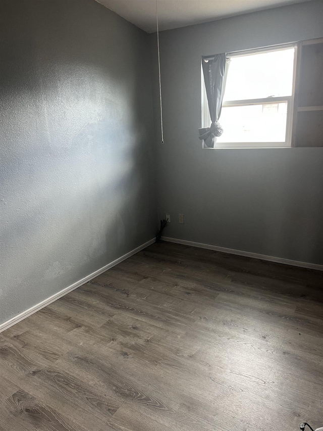 spare room with baseboards and wood finished floors