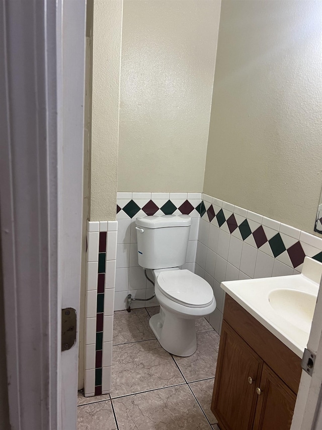 half bath with toilet, tile walls, wainscoting, and vanity