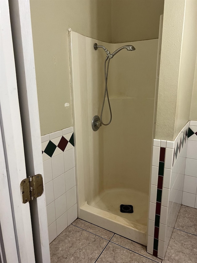 full bath with tile patterned flooring, tile walls, a wainscoted wall, and a shower stall