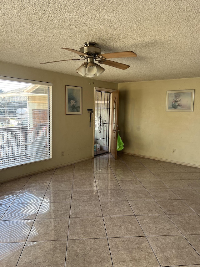 spare room featuring tile patterned floors, baseboards, a textured ceiling, and ceiling fan