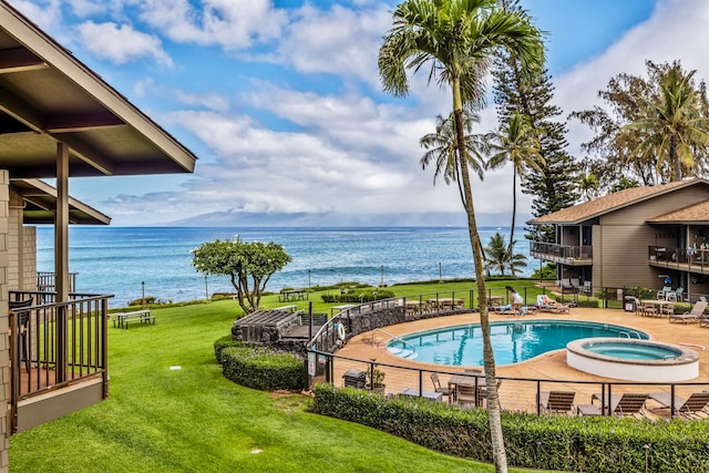 view of pool with a hot tub, a lawn, and a water view