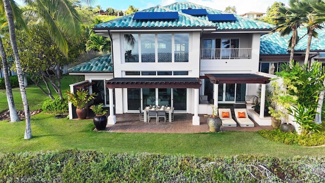 back of property with solar panels, a balcony, a yard, a patio area, and stucco siding