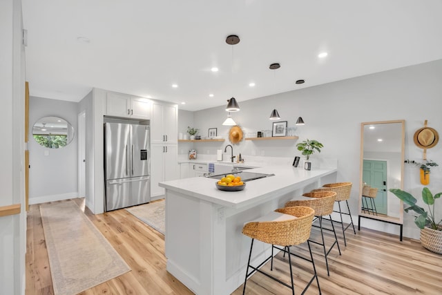 kitchen featuring stainless steel refrigerator with ice dispenser, kitchen peninsula, pendant lighting, a breakfast bar area, and white cabinets