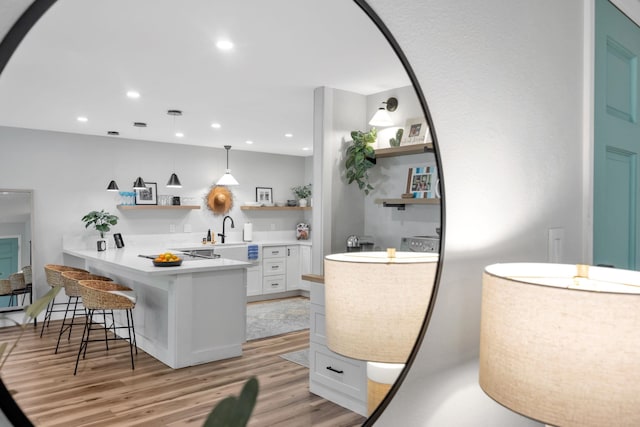 kitchen featuring white cabinets, hanging light fixtures, light hardwood / wood-style flooring, kitchen peninsula, and a breakfast bar area