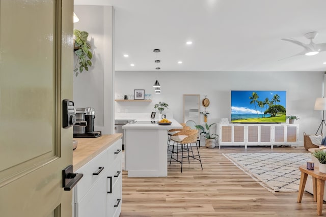 kitchen featuring a kitchen breakfast bar, light wood-type flooring, pendant lighting, a center island, and white cabinetry