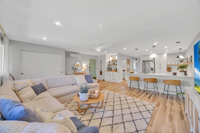 living room with a wall mounted air conditioner, ceiling fan, and light hardwood / wood-style floors